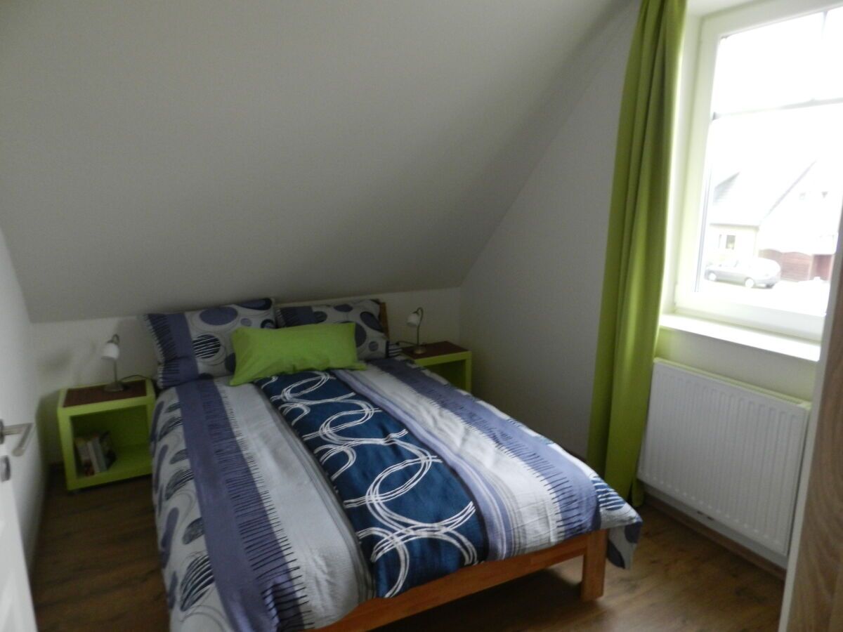 Una habitación pequeña con una cama individual, techo inclinado, ventana con cortinas verdes y un radiador.