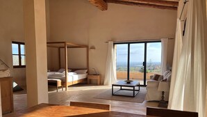 A spacious room with a large bed, a sofa, and a dining table. There is a view of the outdoors through large windows. - Son Pages - two exclusive houses with sea views, large pool, fully air-conditioned (Manacor)