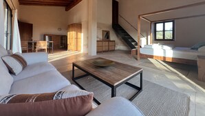 Un vaste espace de vie doté d’un haut plafond, de poutres apparentes, d’un grand lit, d’une table à manger et d’un escalier menant à un niveau supérieur.