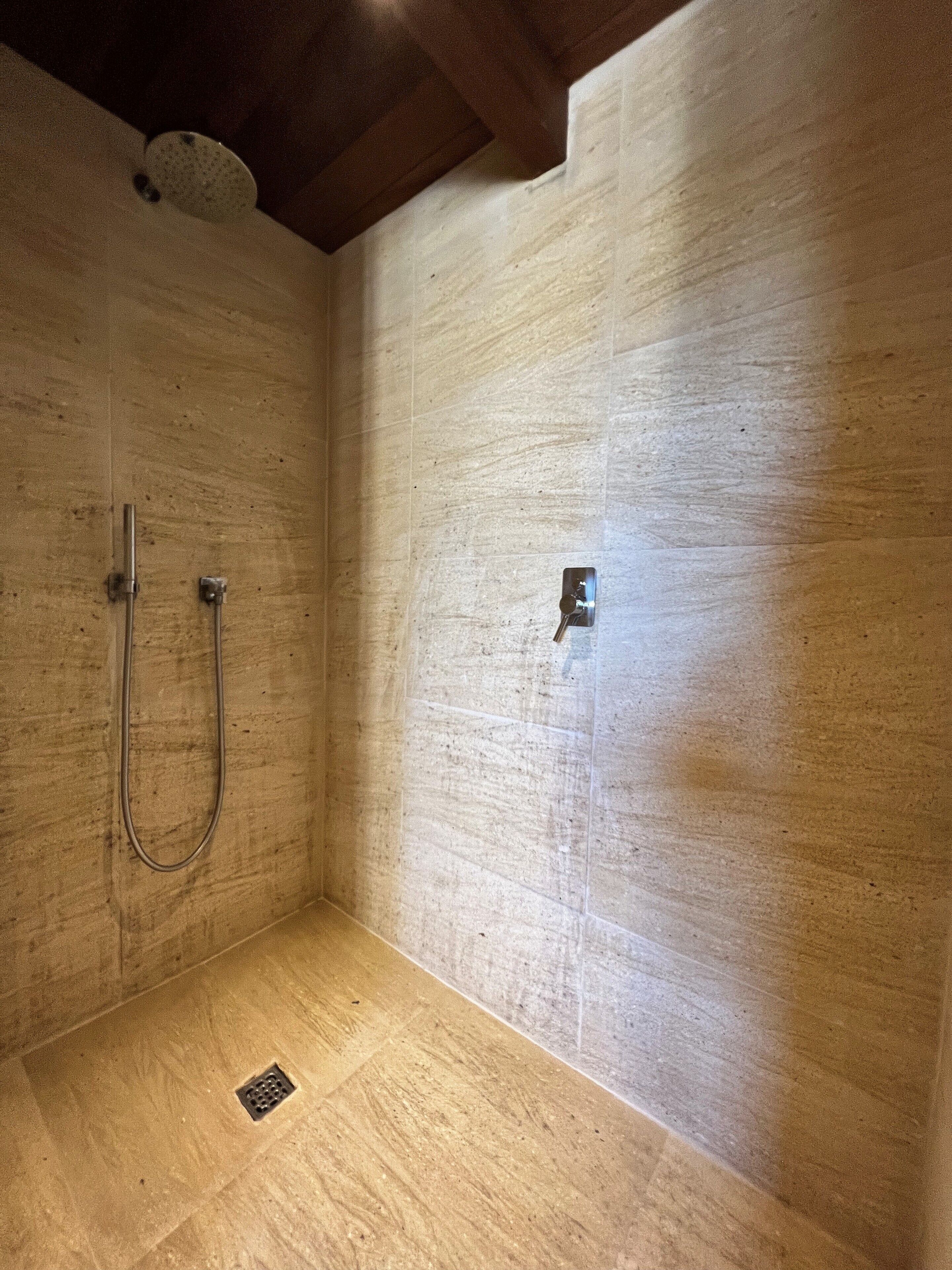 A shower with a metal hose and a control panel on a tiled wall.