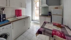 Una cucina funzionale con mobili bianchi, lavatrice, lavello e zona pranzo con tovaglia fantasia.