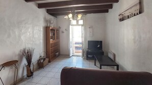 Un soggiorno con un divano, una televisione, una libreria in legno e una ventola.