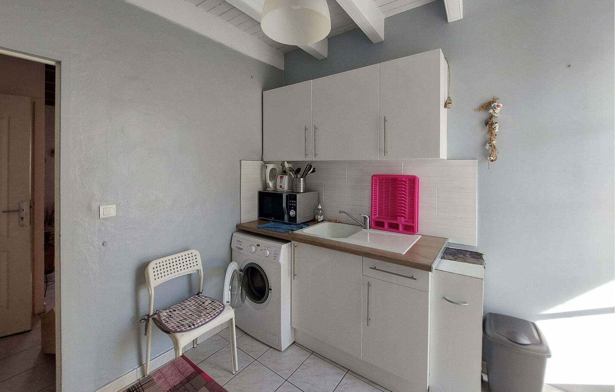 Una cocina compacta con lavadora, un lavabo y una silla.