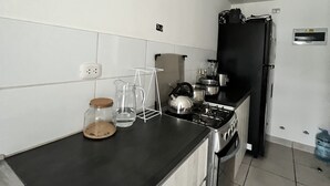 Una cocina con encimera negra, electrodomésticos de acero inoxidable y paredes con azulejos blancos.