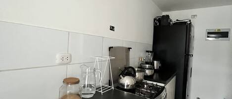 A kitchen with a black countertop, stainless steel appliances, and white tiled walls.
