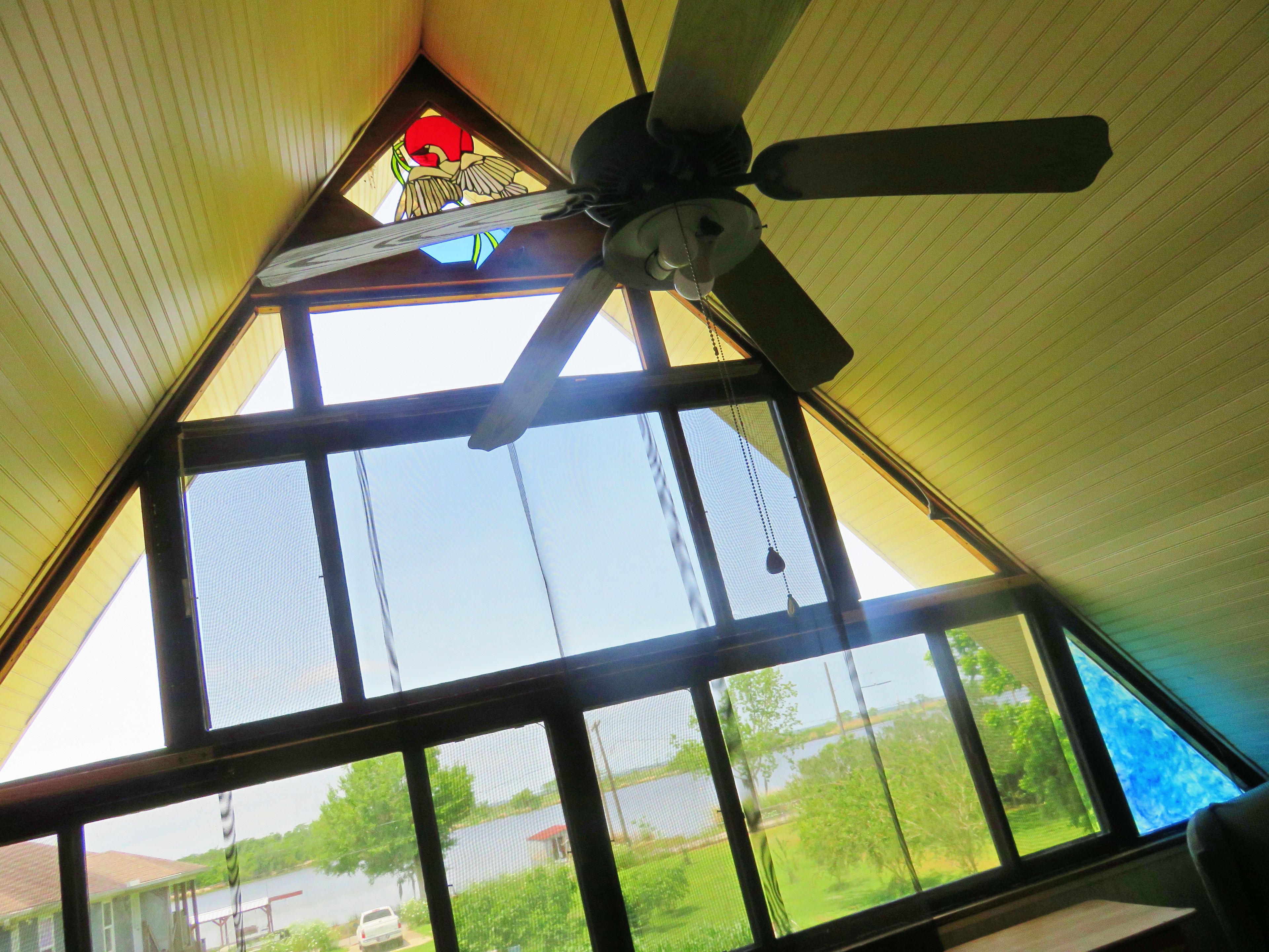Una habitación con ventilador de techo, una ventana de vitral y vistas al agua y vegetación exterior.