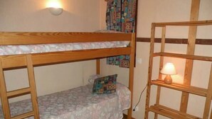 A bunk bed room with a wooden ladder, a bedside table with a lamp, and a patterned bedspread.