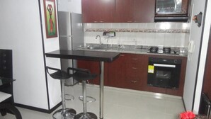 A compact kitchen with a black countertop, stainless steel appliances, and a microwave. There are two stools at the counter. - Emdoralahouse (Cali)