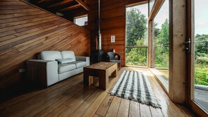 A wooden interior with a sofa, a table, and a view of greenery outside. - Hotel Parque Tepuhueico (Chonchi)