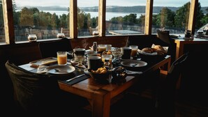 A breakfast table set with various dishes and drinks, overlooking a scenic view of a lake and forest. - Hotel Parque Tepuhueico (Chonchi)