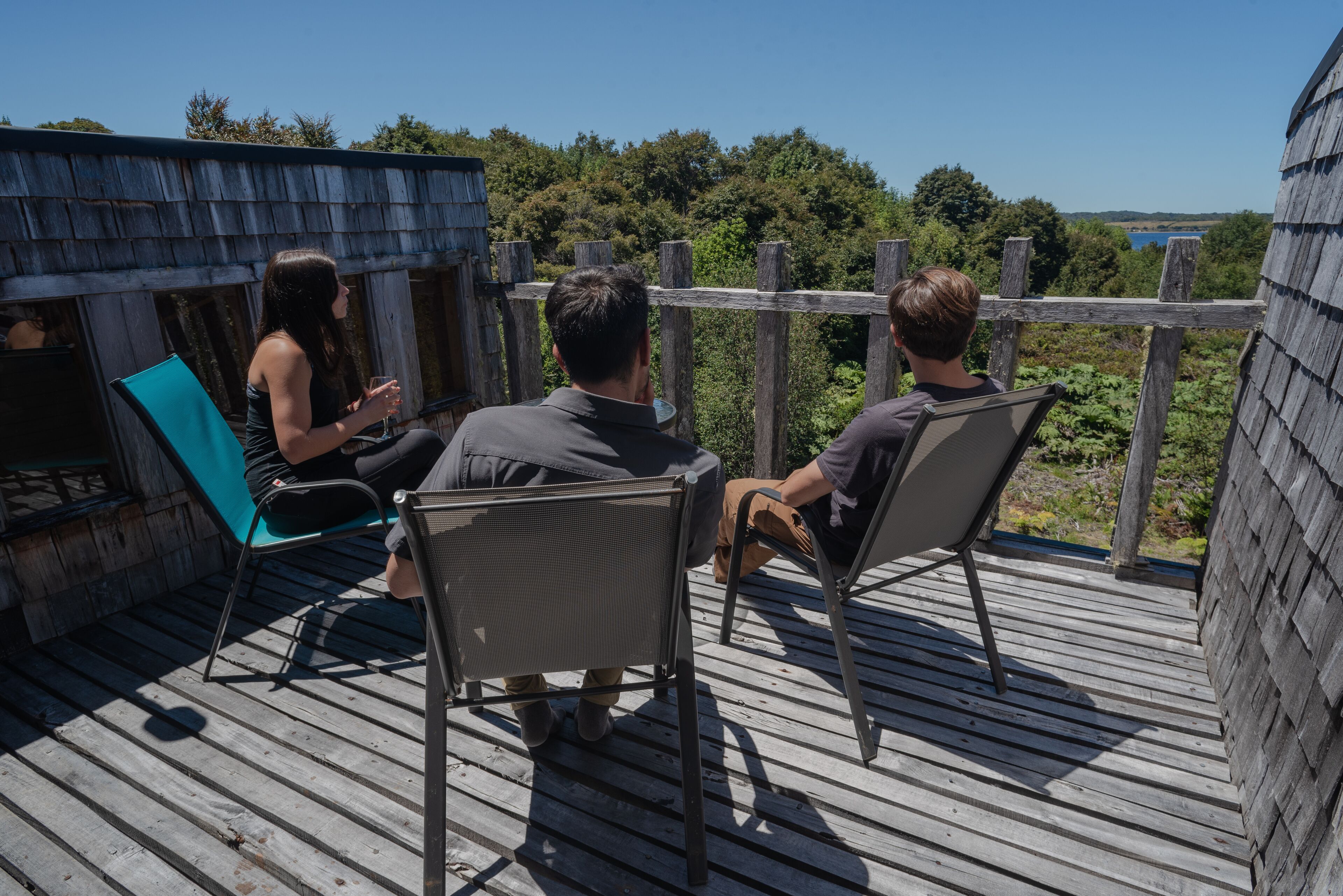 A wooden deck with metal chairs, overlooking a natural landscape with trees and a body of water.