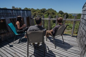 Une terrasse en bois avec des chaises en métal, donnant sur un paysage naturel composé d’arbres et d’une étendue d’eau.