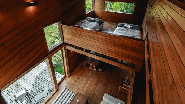 A cabin with a loft-style bedroom, a sofa, and a dining area with a view of the outdoors. - Hotel Parque Tepuhueico (Chonchi)