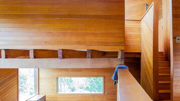 A cabin with two wooden beds, a small wooden desk, and a window with a view of trees.