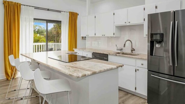 A modern kitchen with white cabinets, a stainless steel refrigerator, and a large island with bar stools. - [lounge like locals] walk to siesta beach +bikes (Siesta Key)