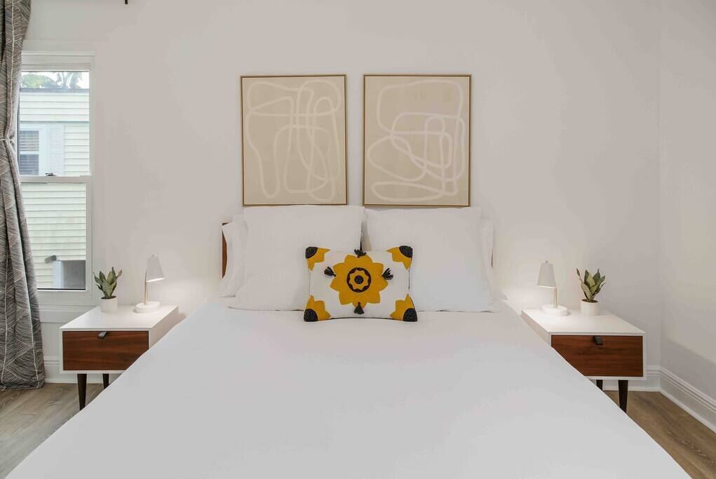A bedroom with a large bed, two bedside tables with lamps, and a window with curtains.
