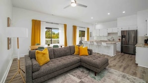 A modern living room with a sectional sofa, a dining area with yellow curtains, a kitchen with white cabinets, and a ceiling fan. - [lounge like locals] walk to siesta beach +bikes (Siesta Key)