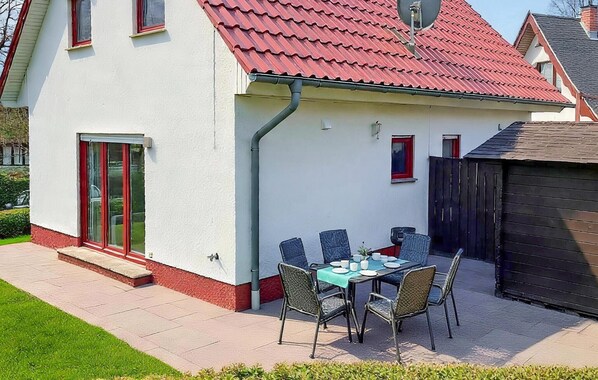 Een huis met een rood pannendak, een witte gevel en een klein terras met een tafel en stoelen.