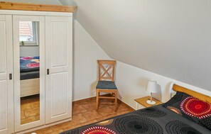 Een slaapkamer met een bed, een stoel, een nachtkastje en een kledingkast.