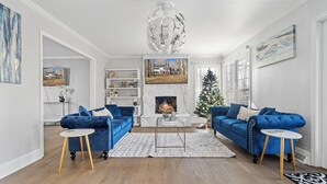 A modern living room with two blue sofas, a fireplace, a Christmas tree, and a large globe chandelier.