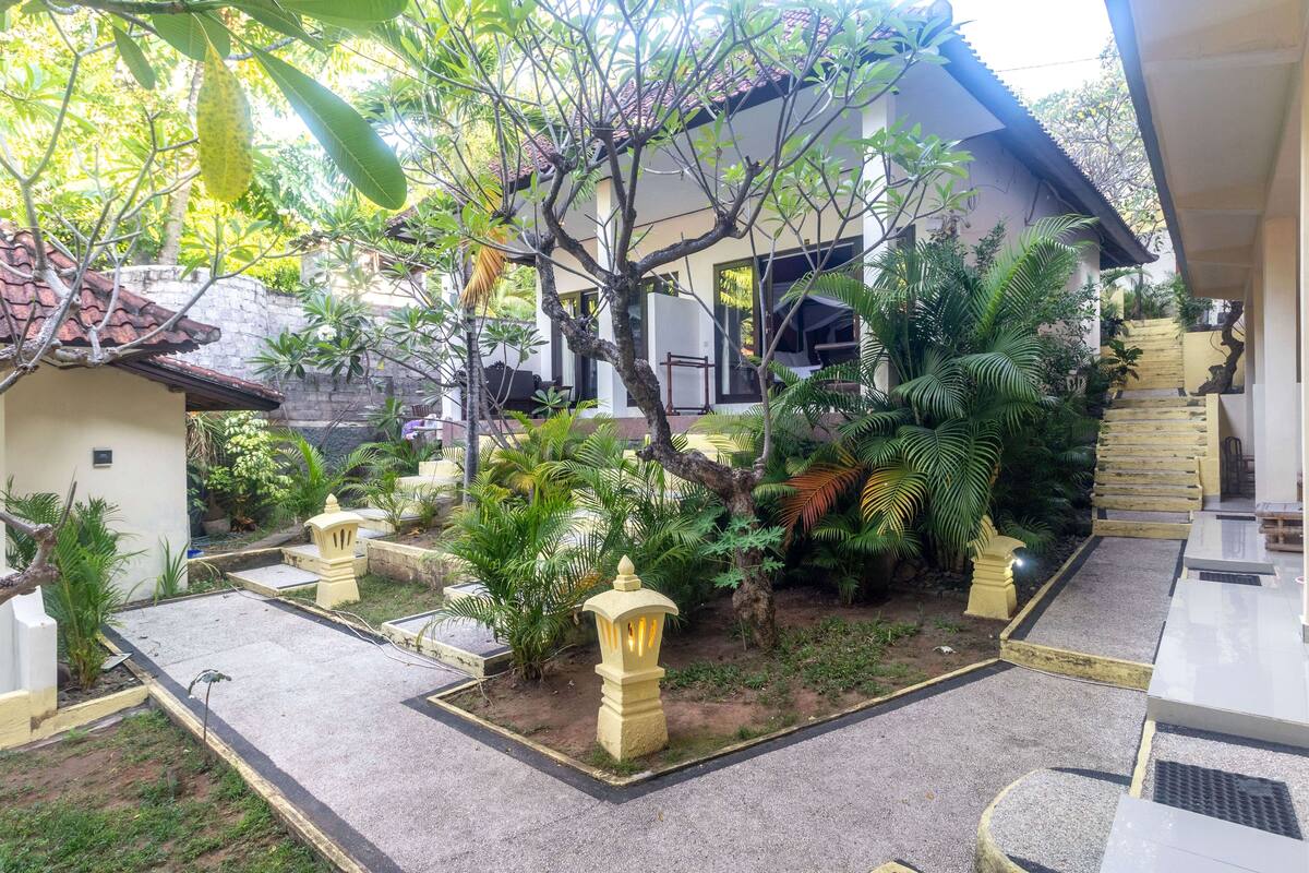 Un patio con un árbol, un edificio blanco y una escalera.