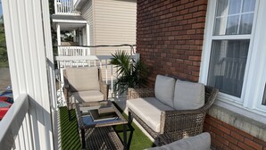 Un patio con mobiliario de mimbre, una mesa de centro de vidrio y una pequeña zona verde.
