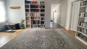 Una habitación amplia con un gran tapete estampado, una estantería llena de libros y una planta en maceta.