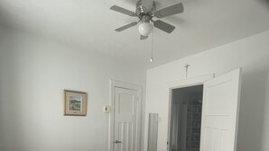 Un dormitorio con dos camas, un ventilador de techo, una puerta y un cuadro en la pared.