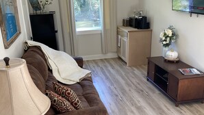 Un soggiorno con un divano marrone, un tavolino in legno, una televisione, un armadio e una finestra con tende.