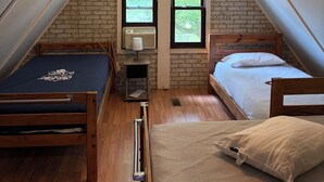 Un dormitorio tipo loft con techo inclinado, dos camas, una mesita y un ventanal.