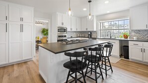 A modern kitchen with white cabinetry, a central island with bar stools, a large window, and a herringbone backsplash.