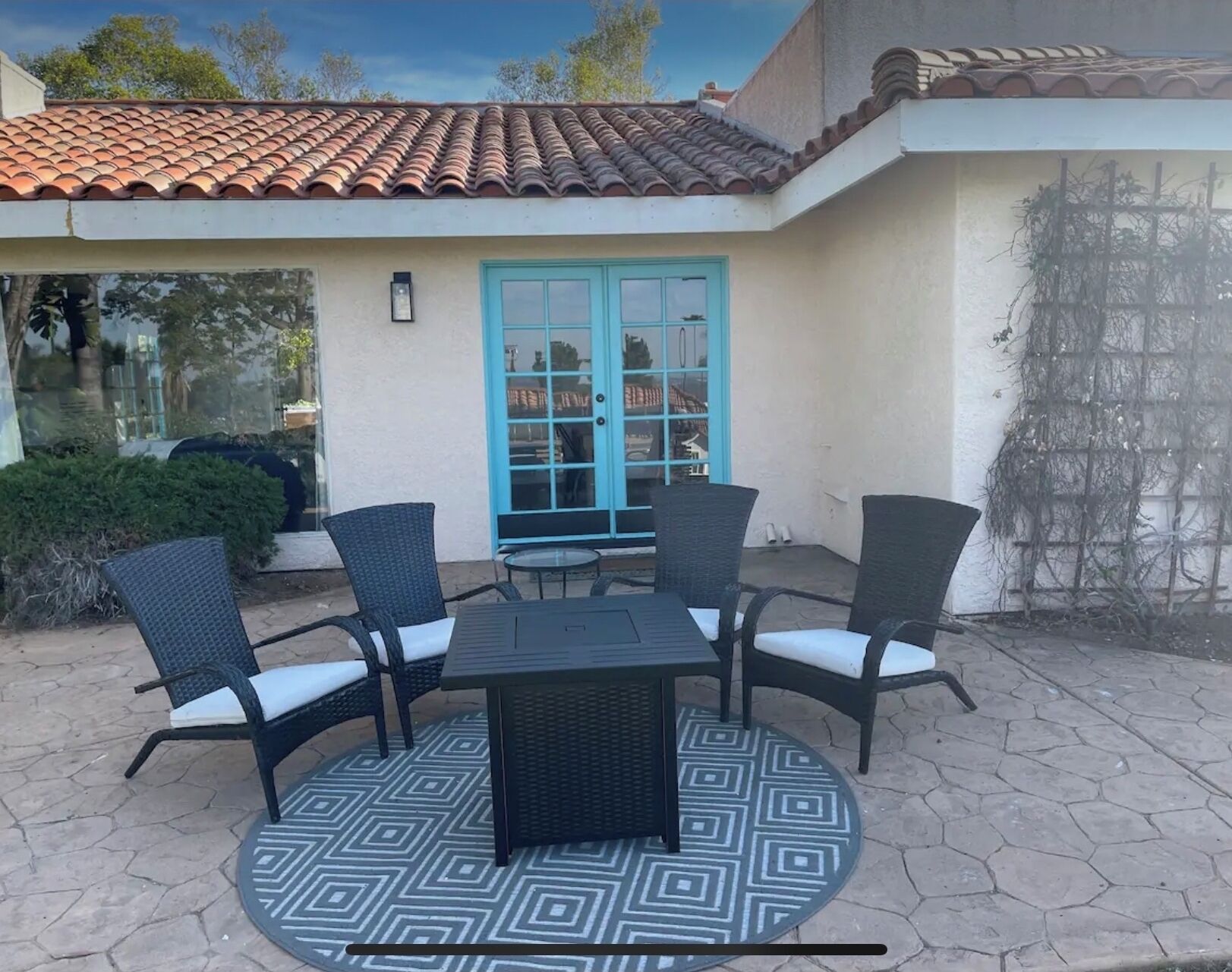 A patio with a round table and four chairs, a blue door, and a tiled roof.