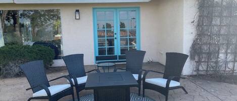 A patio with a round table and four chairs, a blue door, and a tiled roof.