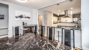 Een moderne keuken met een zwarte marmeren aanrecht, witte kasten en een accentmuur van baksteen.