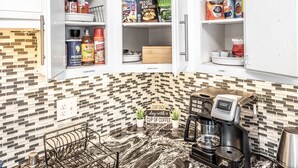 Een keuken met een marmeren aanrecht, een koffieapparaat en open kastjes met diverse etenswaren en kruiden.