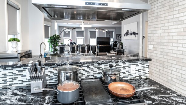 Een moderne keuken met een zwart-wit betegelde achterwand, roestvrijstalen apparatuur en een grote afzuigkap.