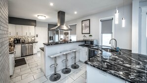 Een moderne keuken met een centraal eiland, roestvrijstalen apparatuur en een zwart marmeren aanrecht.