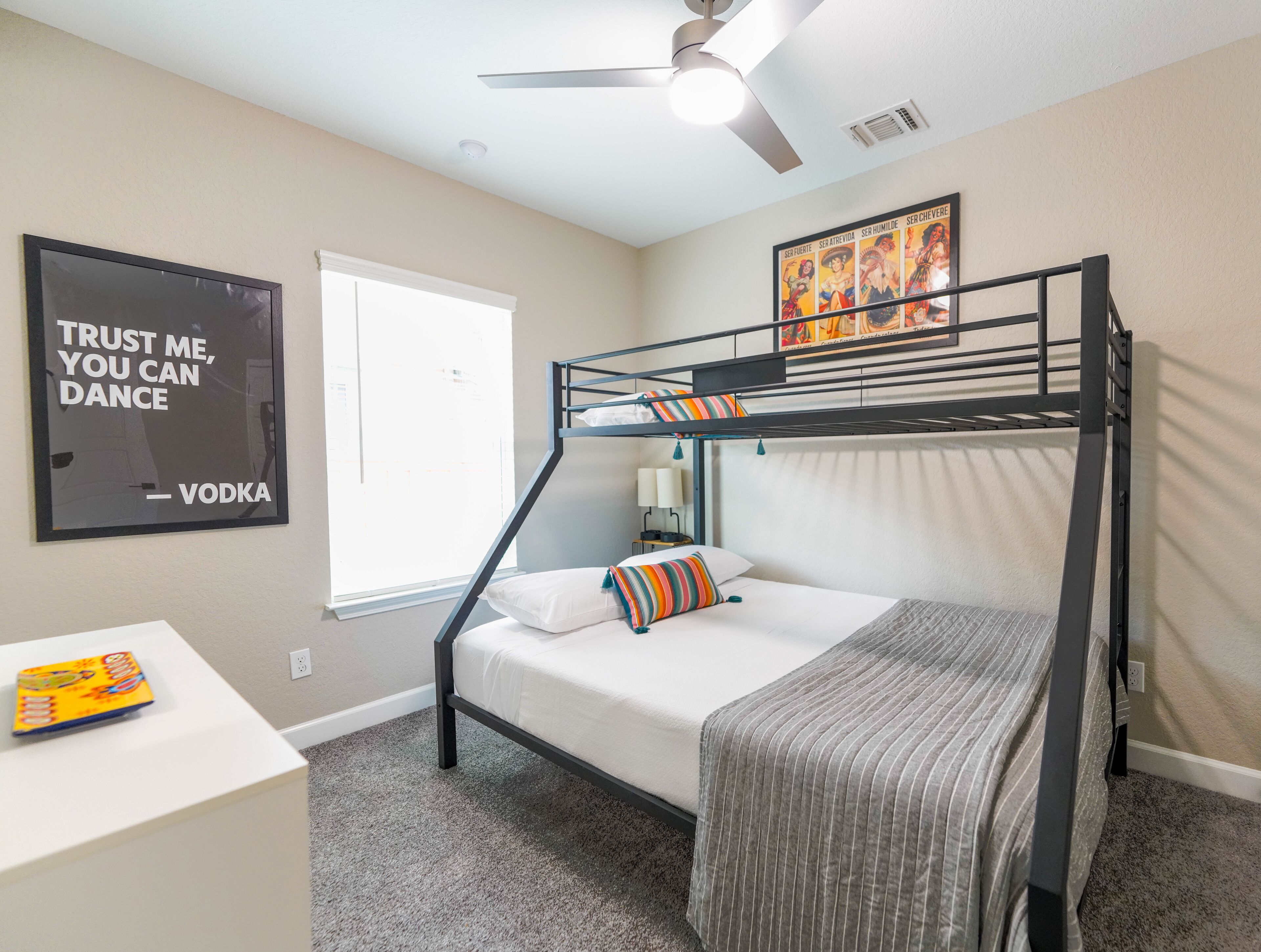 A bunk bed room with a ceiling fan, a poster on the wall, and a window with blinds.