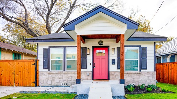 Une maison à deux étages avec une porte d’entrée rouge, des fondations en pierre et une clôture en bois.