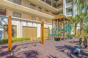A playground with swings and a climbing structure, surrounded by a building with balconies.
