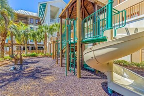 A playground with a slide, climbing structures, and palm trees.
