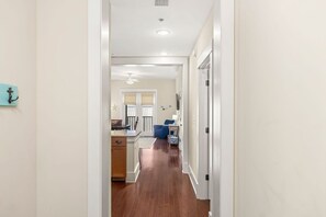A hallway leading to a kitchen and living area with wooden flooring, white walls, and a ceiling fan. - Redfish Village - Beach Please - 2BR/2BA - Gulf Views - Seasonal Beach Tram (Santa Rosa Beach)