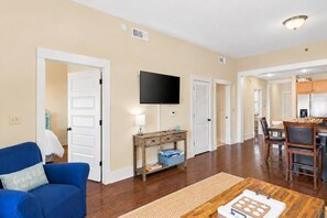 A living room with a blue sofa, a coffee table, and a flat-screen TV mounted on the wall.