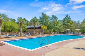 A swimming pool with lounge chairs and umbrellas, surrounded by trees and a fenced area.