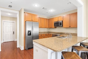 A kitchen with wooden cabinets, stainless steel appliances, a granite countertop, and a built-in island with bar stools.