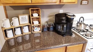 Ett kök med träskåp, en bänkskiva i granit, en kaffebryggare, muggar och en skylt med texten: ”Kan inte bestämma mig för om jag behöver en kopp kaffe eller en hel veckas sömn.”