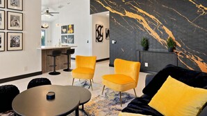 Un espace de détente moderne avec un mur en marbre, des chaises jaunes, un canapé noir et un petit coin bar.