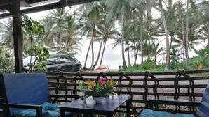 A covered outdoor seating area with a table and chairs, overlooking a beach with palm trees. - Island Hopper Hotel (Kosrae)