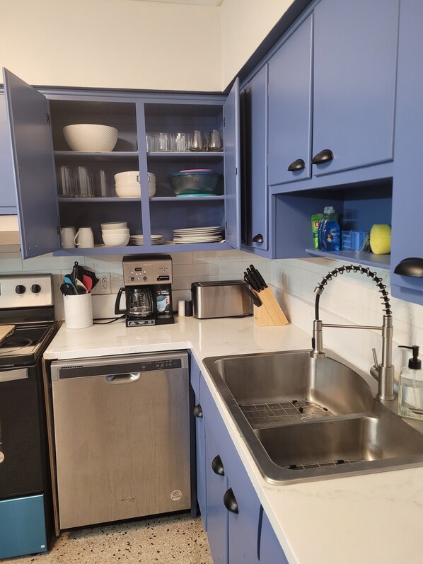 Una cocina compacta con lavavajillas, cafetera y lavabo.