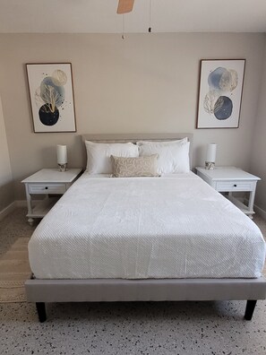 A large bed with white bedding, two bedside tables with lamps, and two framed artworks on the walls.
